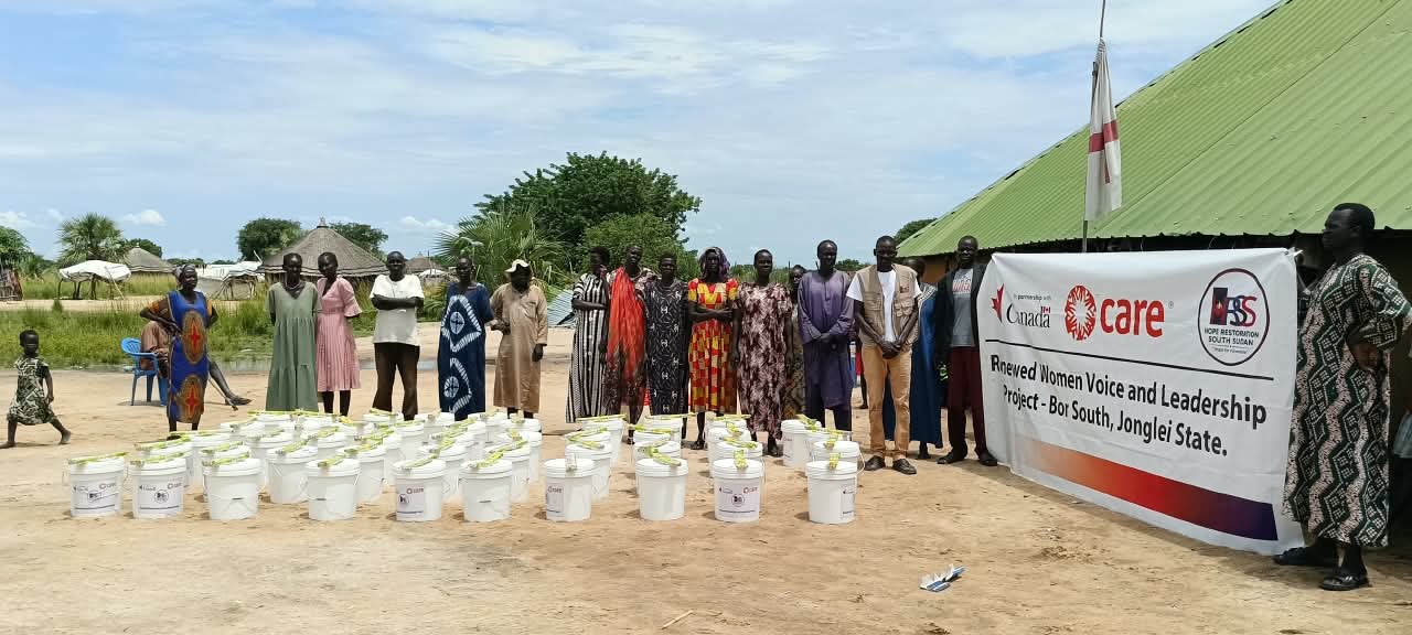 Participants and HRSS staff with the WASH items in front of the project banner.