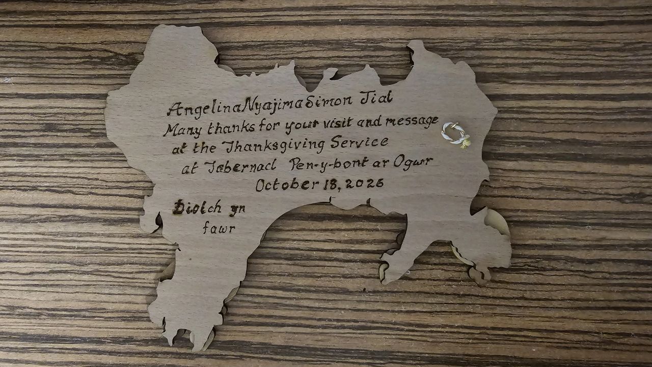 A wooden map of Wales engraved with a thank-you message to Angelina Nyajima Simon Jial for her visit and message at the Thanksgiving Service at Tabernacl on 18 October 2026, ending with “Diolch yn fawr”.
